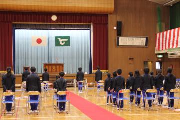 体育館に並んだパイプ椅子の前で起立する生徒達